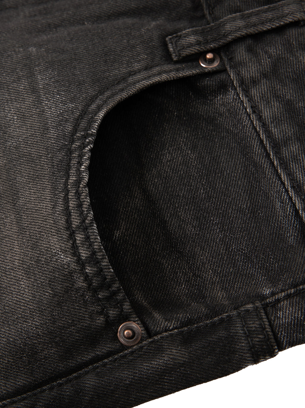 Close-up of vintage wash black heavyweight denim jeans showing pocket detail and copper-toned metal rivets.